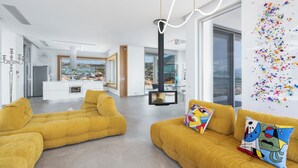 A modern living room with mustard-colored sofas, a fireplace, and a large window overlooking a scenic landscape.