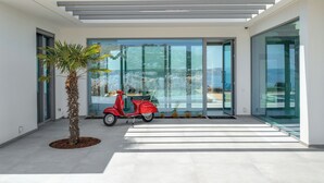 A modern house with a glass door leading to a balcony, a red scooter parked outside, and a palm tree in the foreground.