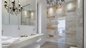 A modern bathroom with a stone wall, a glass shower enclosure, and a white sink with towels.