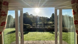 Ein Zimmer mit Blick auf einen Rasen und einen Teich durch eine Glastür.