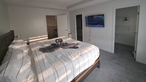 Een slaapkamer met een bed, een televisie aan de muur en een deur naar een andere kamer.