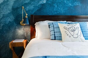Ein Schlafzimmer mit einem hölzernen Kopfende, einem Nachttisch mit Lampe und zwei Kissen mit Text und Handabdruck-Muster.