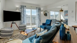 A modern living room with a large TV, comfortable seating, a wooden coffee table, and a view of the outdoors. - Ocean Paradise Awaits. 2 bed 1 bath, Walking distance to the ocean! (Avila Beach)