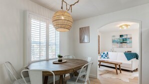 Un comedor con una mesa redonda de madera, sillas blancas y una lámpara colgante de fibras naturales.
