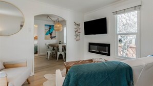 Una sala de estar moderna con un sofá, una zona de comedor y un televisor montado en la pared.