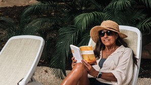 A person sitting on a white lounge chair outdoors, reading a book.