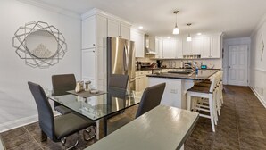 Una cocina moderna con armarios blancos, electrodomésticos de acero inoxidable y una mesa de comedor de vidrio.
