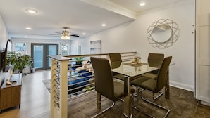 Un comedor moderno con una mesa de vidrio y sillas de metal, un ventilador de techo y un elemento decorativo en la pared.