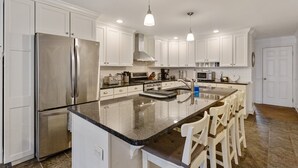 Una cocina moderna con armarios blancos, electrodomésticos de acero inoxidable, encimera de granito e iluminación colgante.