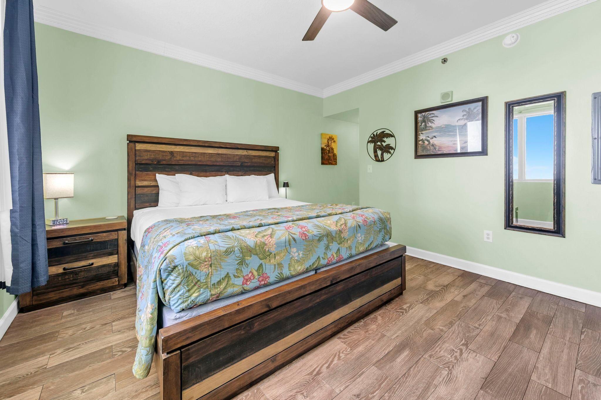 Un dormitorio con una cama, mesitas de noche de madera, un ventilador de techo y una ventana.