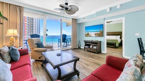 A hotel room with a balcony, a bed, a seating area with a table, and a TV. - Shores of Panama 816 (Panama City Beach)