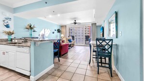 A modern kitchen with a central island, a dining area with a red sofa, and a balcony with a view. - Shores of Panama 816 (Panama City Beach)