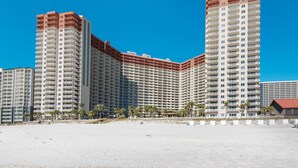 A high-rise hotel with multiple balconies, a beach in the foreground, and palm trees. - Shores of Panama 816 (Panama City Beach)