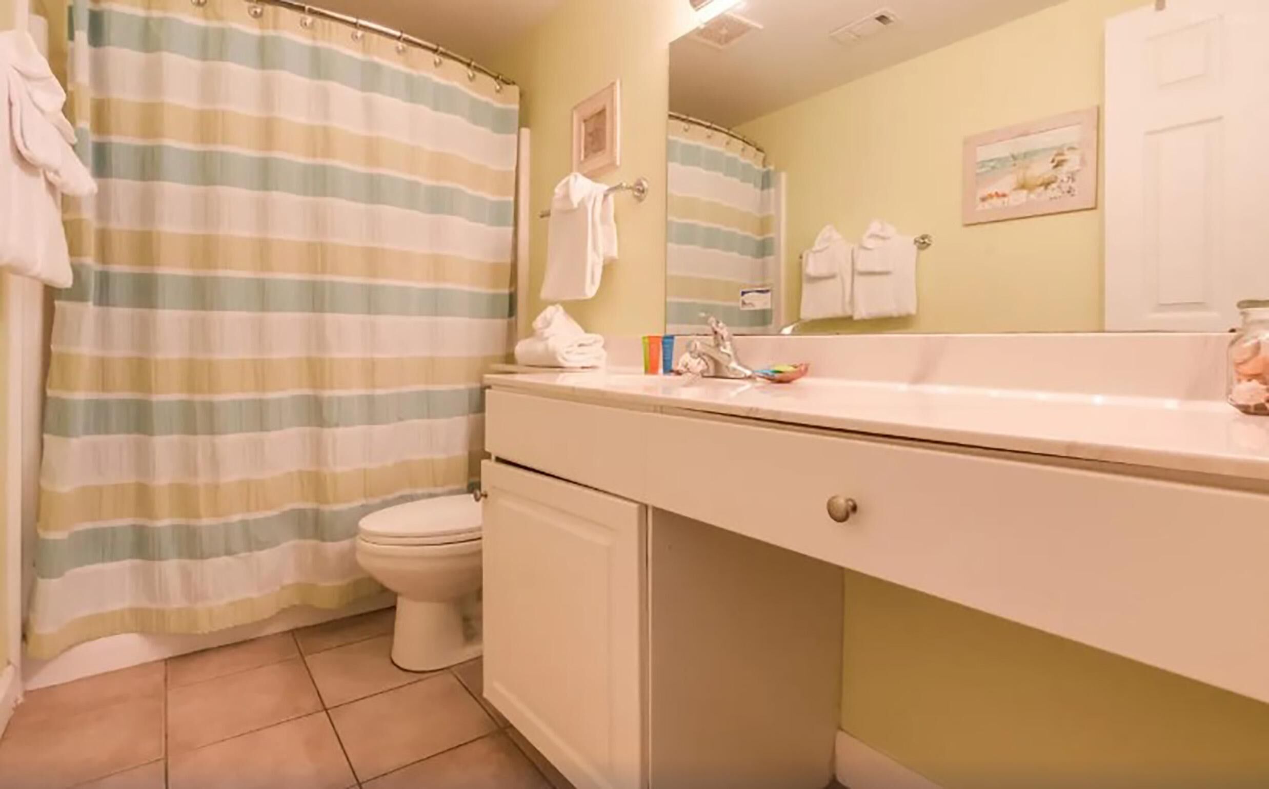 Une salle de bain avec un rideau de douche à rayures, des toilettes, un lavabo avec un miroir et un meuble de rangement.