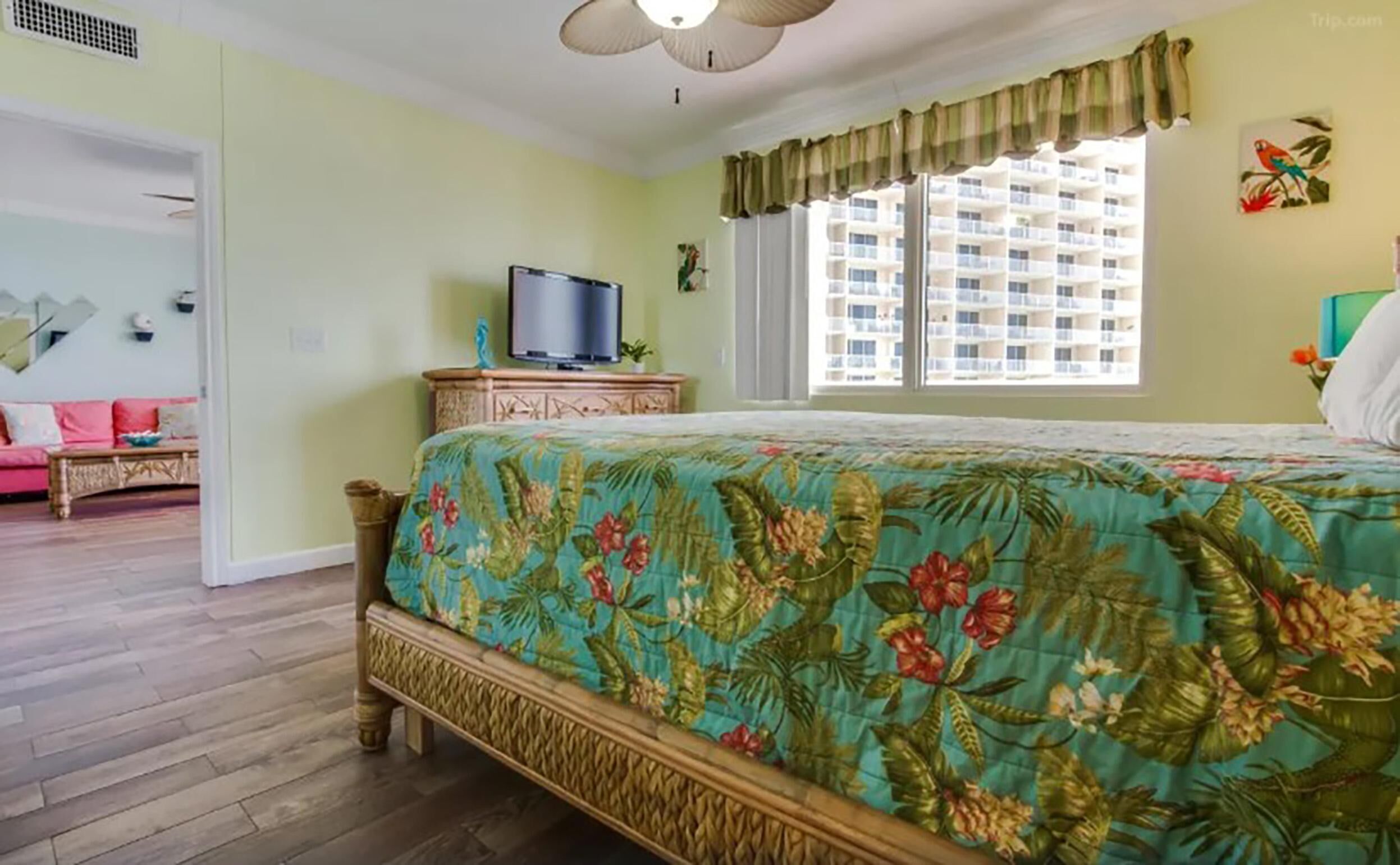 A bedroom with a bed, a television on a wooden cabinet, a window with curtains, and a view of a building outside.