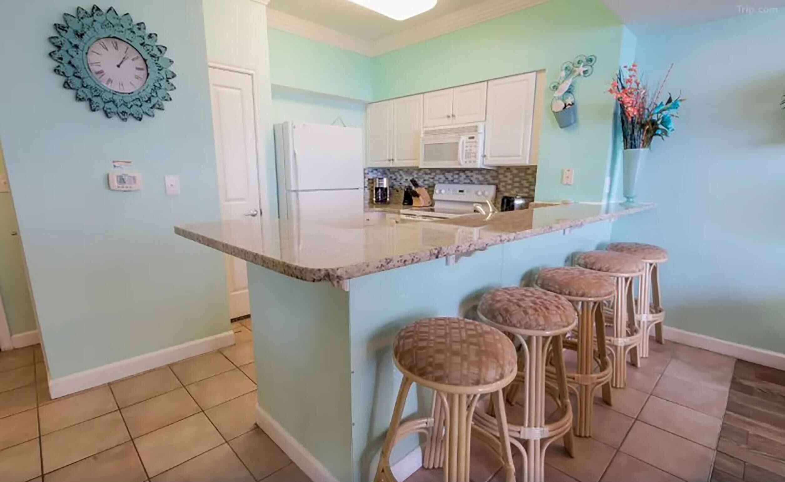 A kitchen with a bar area, white cabinets, a refrigerator, and a decorative clock.