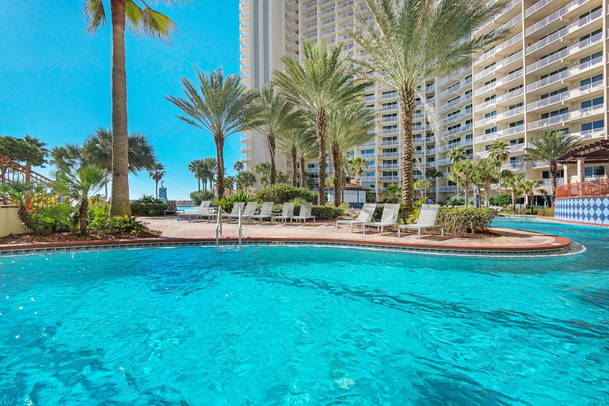 A pool area with clear blue water, surrounded by palm trees and lounge chairs.