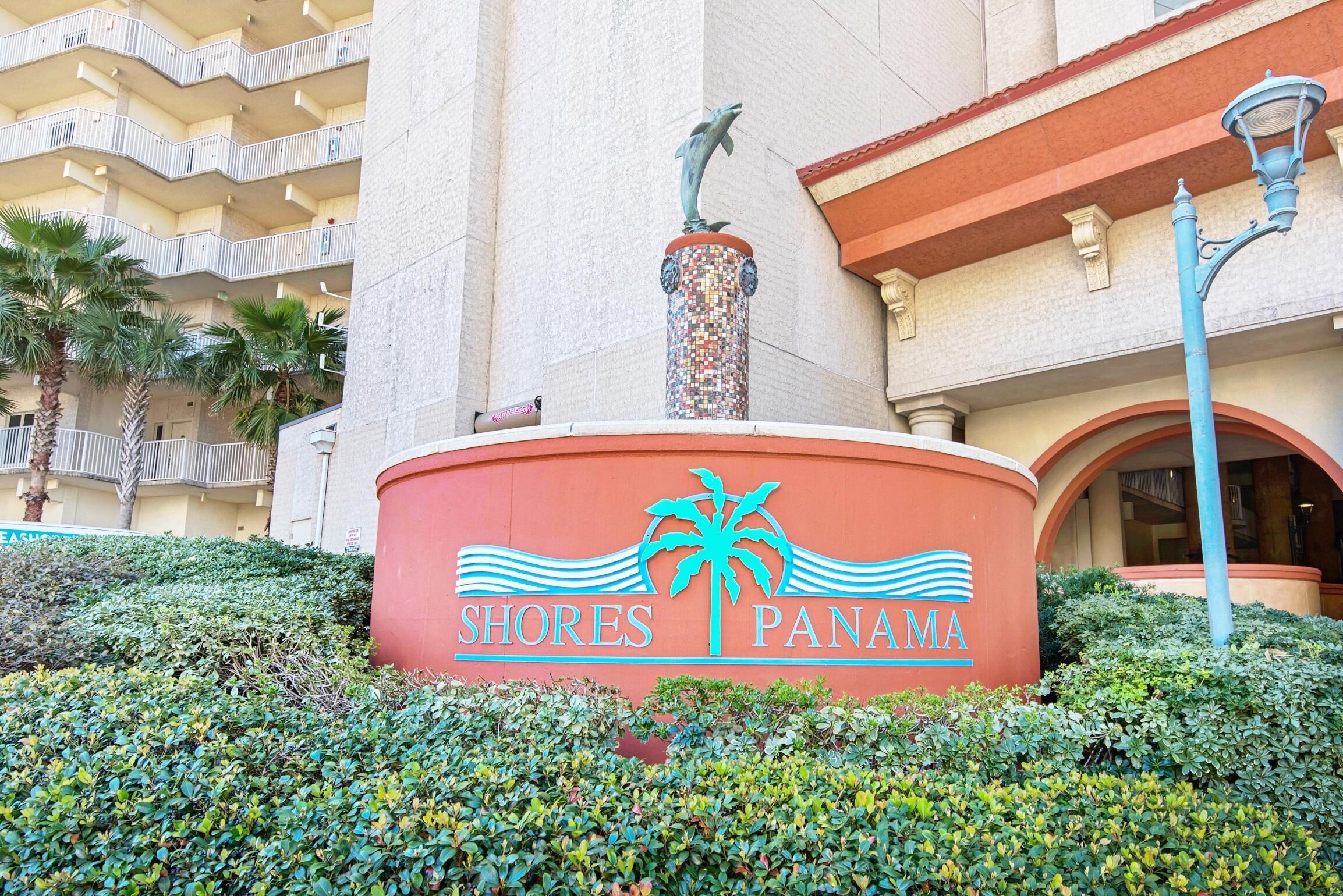 A sign for 'Shores Panama' with a palm tree and waves design, a dolphin statue, and a building with balconies and a red awning.