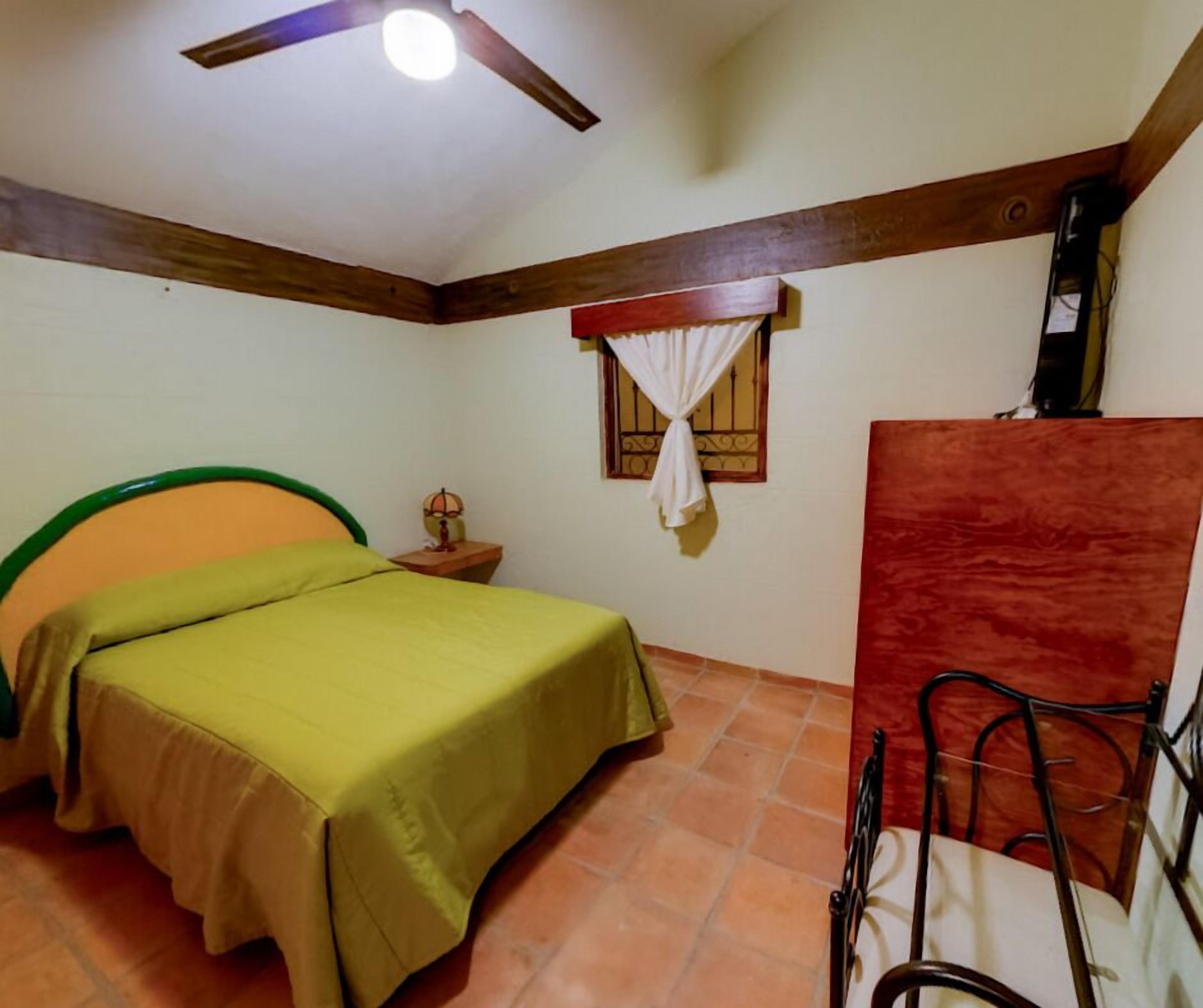 Ein Schlafzimmer mit einem Bett, einem Nachttisch, einem Fenster mit Vorhängen, einem Deckenventilator und einem roten Wandpaneel.
