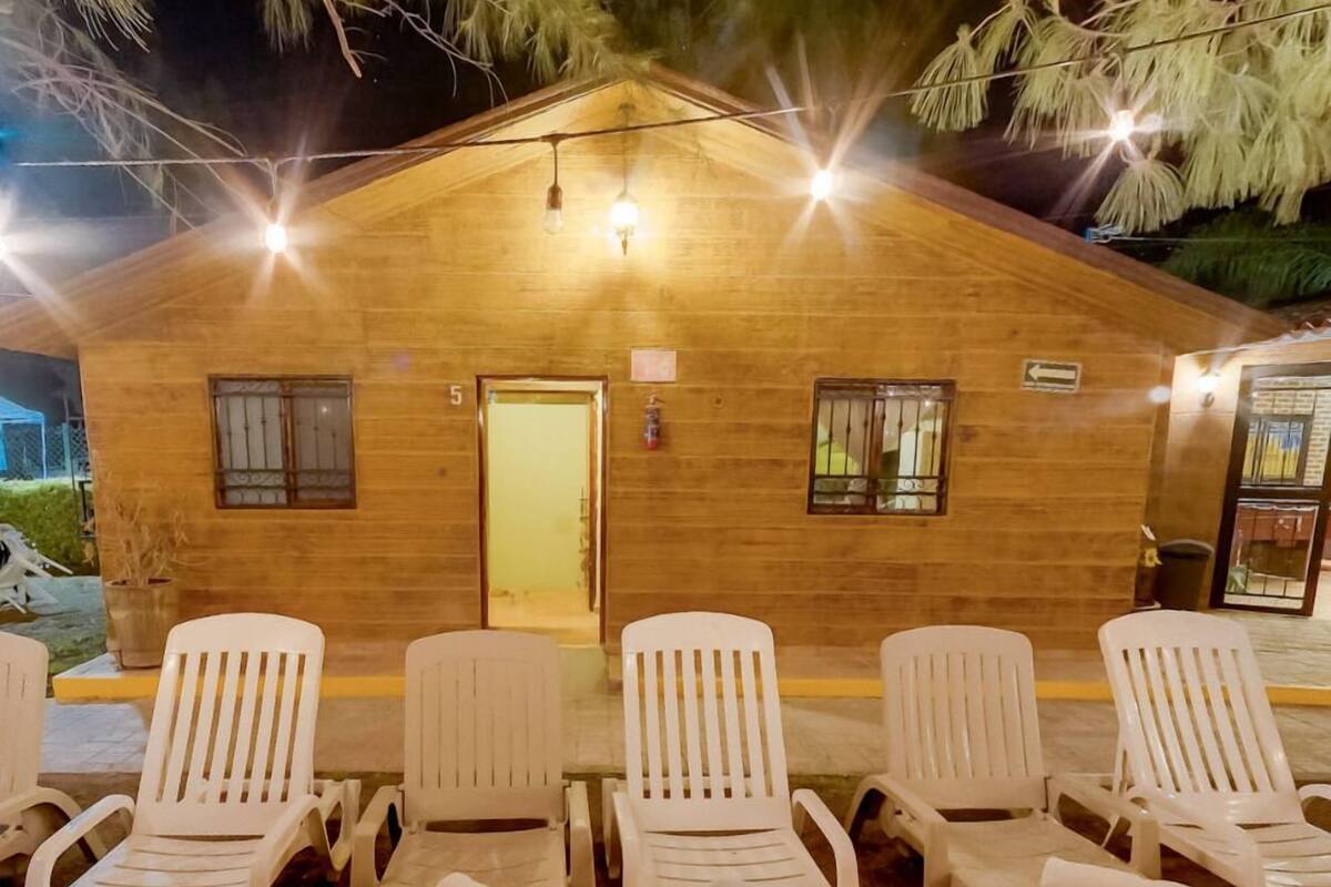 A wooden building with a door and windows, numbered 5, with white plastic chairs and towels in front.