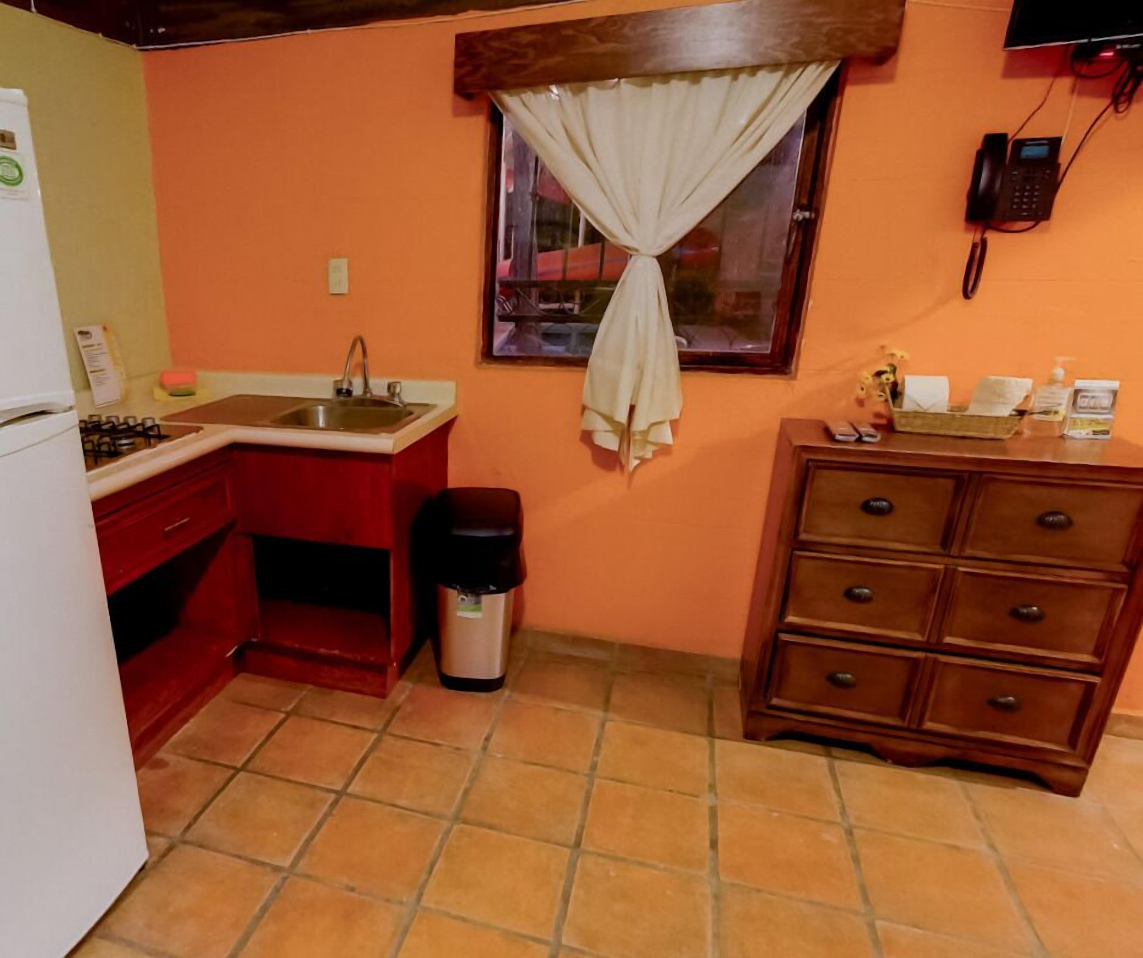 A compact kitchen with a sink, stove, and a small window with a curtain.