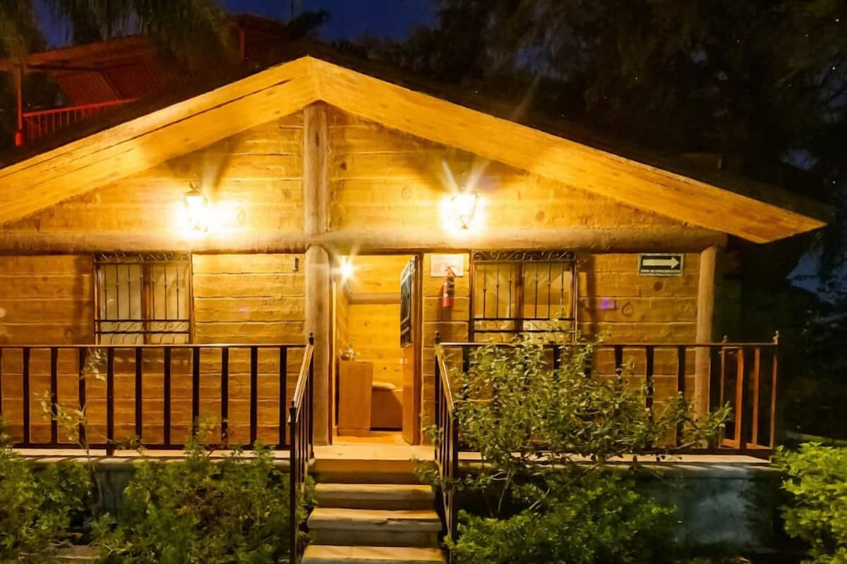 A wooden cabin with a porch, steps leading to the entrance, and a small garden area.