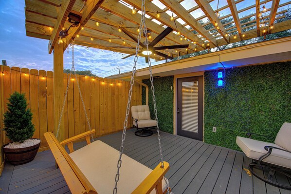 Une terrasse en bois avec un fauteuil suspendu, un banc rembourré et une petite plante en pot.