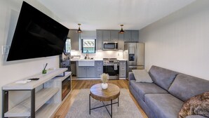 A modern living room with a grey sofa, a coffee table, and a flat-screen TV mounted on the wall. - Charming 1-Bedroom Guest House Near NRG with a Level 2 Fast EV Charger (Houston)