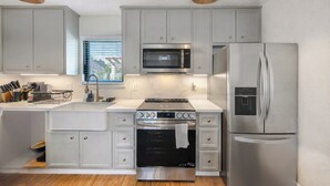A modern kitchen with grey cabinets, stainless steel appliances, and pendant lighting. - Charming 1-Bedroom Guest House Near NRG with a Level 2 Fast EV Charger (Houston)