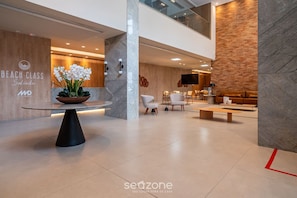 Un hall d’hôtel moderne doté d’un comptoir d’accueil, d’un espace salon et d’un grand écran.