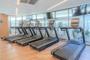 Une salle de sport avec des tapis de course alignés en rangée, de grandes fenêtres et un mur en bois.