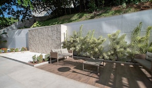 Un espace patio agrémenté d’un mur en pierre, d’un canapé en osier, d’une table en métal et de plantes en pot.