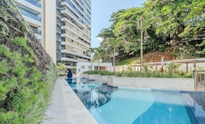 Un edificio moderno con piscina, rodeado de vegetación y un cielo despejado.