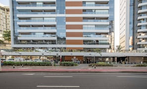 Un hôtel à plusieurs étages au design moderne, caractérisé par un imposant panneau vertical en bois, de grandes fenêtres et un espace d’entrée couvert doté d’un coin salon extérieur.