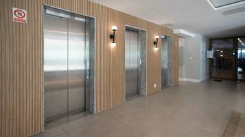 Un área de ascensores moderna con tres elevadores, paneles de madera en las paredes y piso de baldosas.