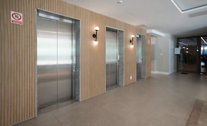 Un área de ascensores moderna con tres elevadores, paneles de madera en las paredes y piso de baldosas.