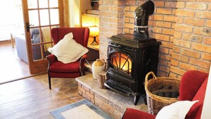 Ein gemütlicher Raum mit Kamin aus Ziegelsteinen, einem roten Sessel, einem Korbwäscher und einem Holzboden.