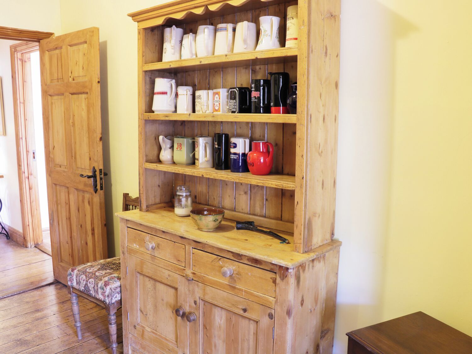Un meuble en bois doté de plusieurs étagères, contenant des ustensiles de cuisine, et une petite table sur laquelle se trouvent un bol et un pot.