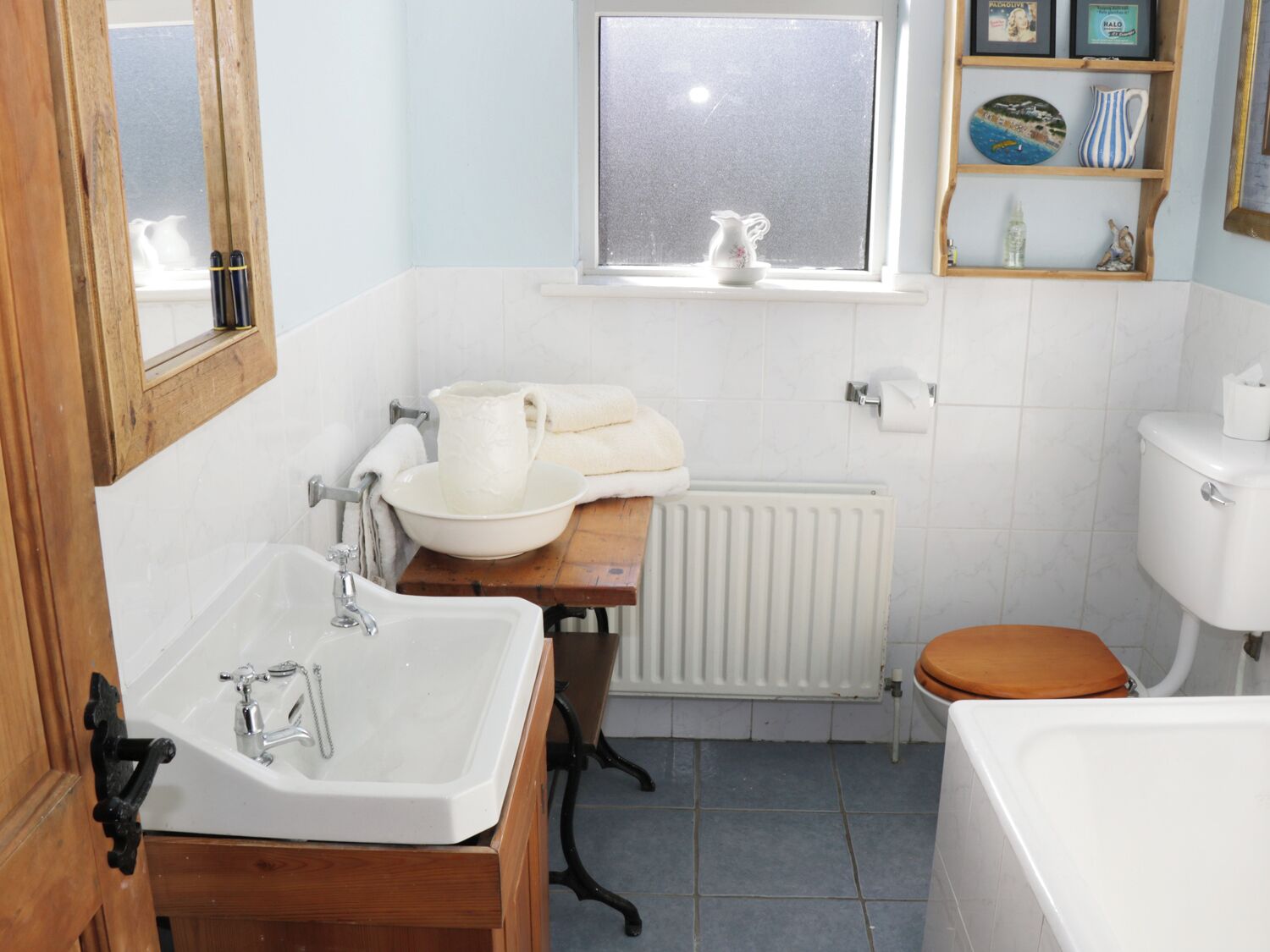 Une salle de bain avec un lavabo blanc, un meuble-lavabo en bois, des toilettes et une fenêtre donnant sur un beau paysage.