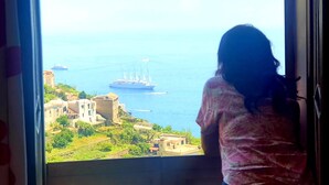 Vista desde una ventana con vista a la costa, edificios y un barco grande a lo lejos.