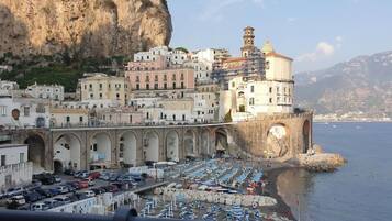 Una cittadina costiera con un edificio storico imponente, un porto turistico con imbarcazioni e uno sfondo di scogliere rocciose.