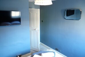 Una habitación con una televisión de pantalla plana montada en la pared, una puerta y un espejo pequeño.