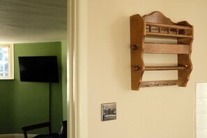 Une pièce avec un mur vert, un téléviseur fixé au mur, une étagère en bois et un interrupteur.