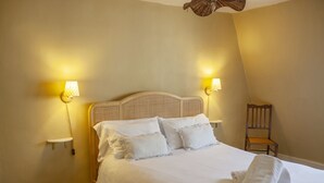 A neatly made bed with white linens and pillows, two wall-mounted lamps, and a wooden chair.