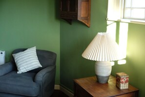 Una habitación con una pared verde, un sillón gris con un cojín a rayas, una mesita de noche de madera con una lámpara y una caja decorativa.