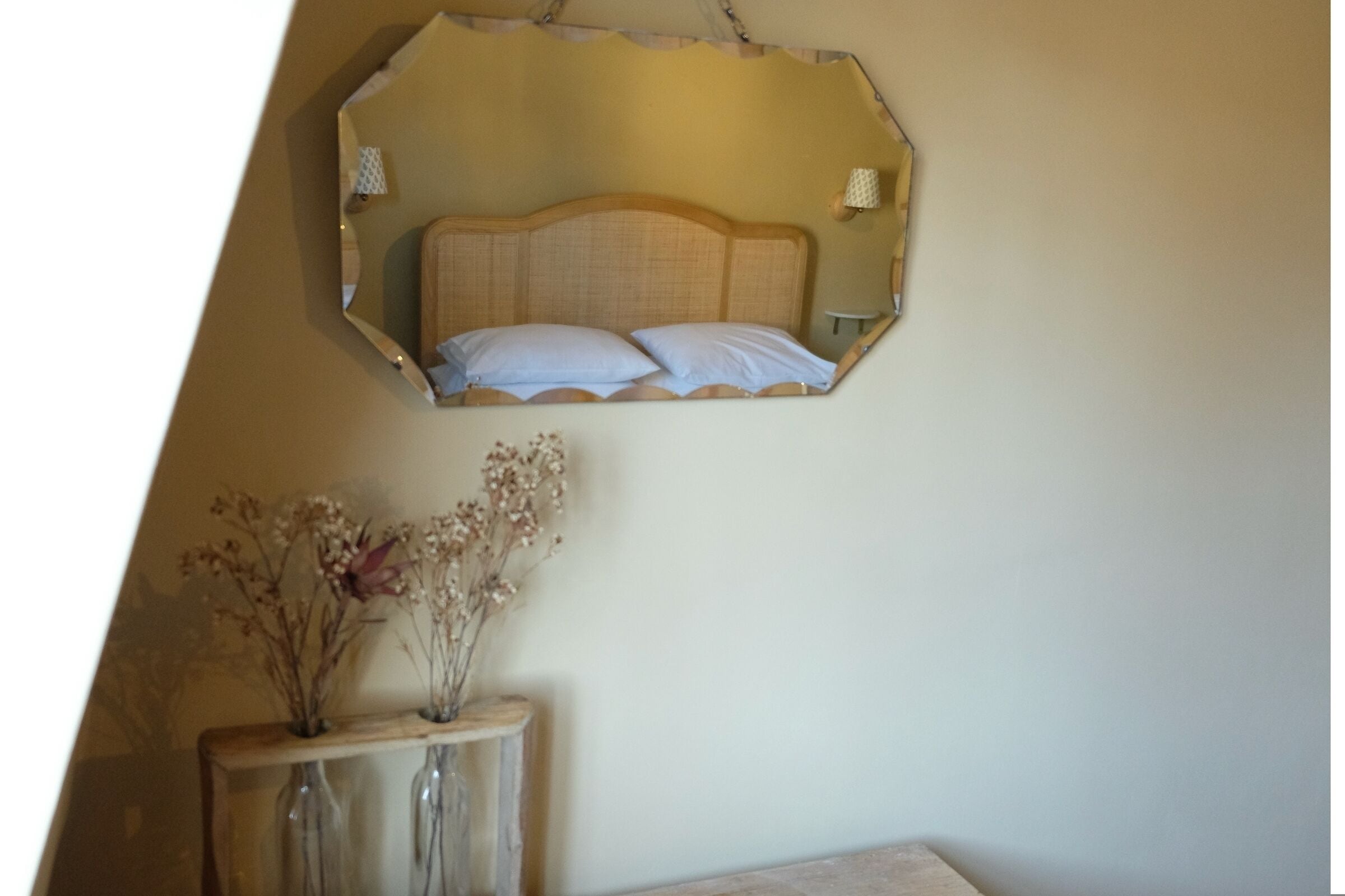 Ein Schlafzimmer mit einem Bett, einem Nachttisch mit einer Vase und einem Spiegel an der Wand.
