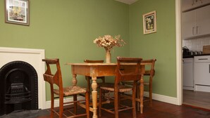 A dining area with a wooden table and chairs, a vase with dried flowers, and a fireplace.