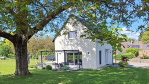 Ein modernes Haus mit Terrasse, Whirlpool und einem Baum im Vordergrund.