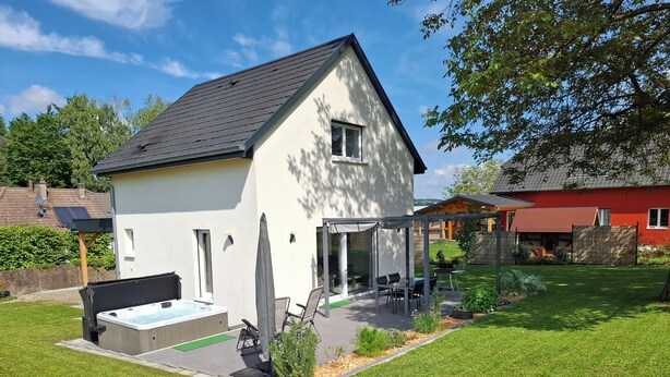 Ein modernes, zweistöckiges Haus mit überdachter Terrasse, Whirlpool und gepflegtem Rasen.