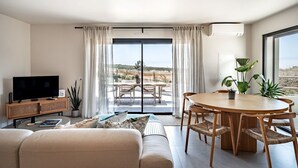 A modern living room with a flat-screen TV, sofa, dining table, and chairs.